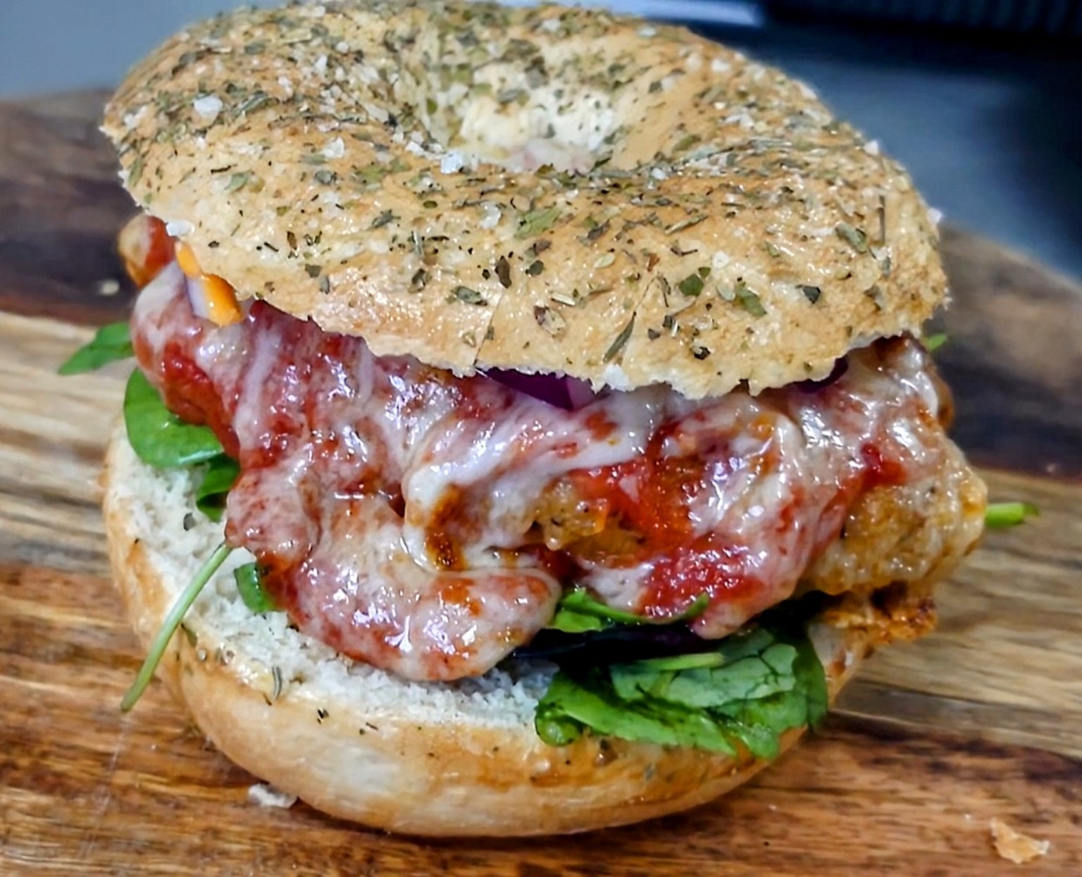 A generously filled herb-topped bagel with melted cheese, tomato sauce and leafy greens