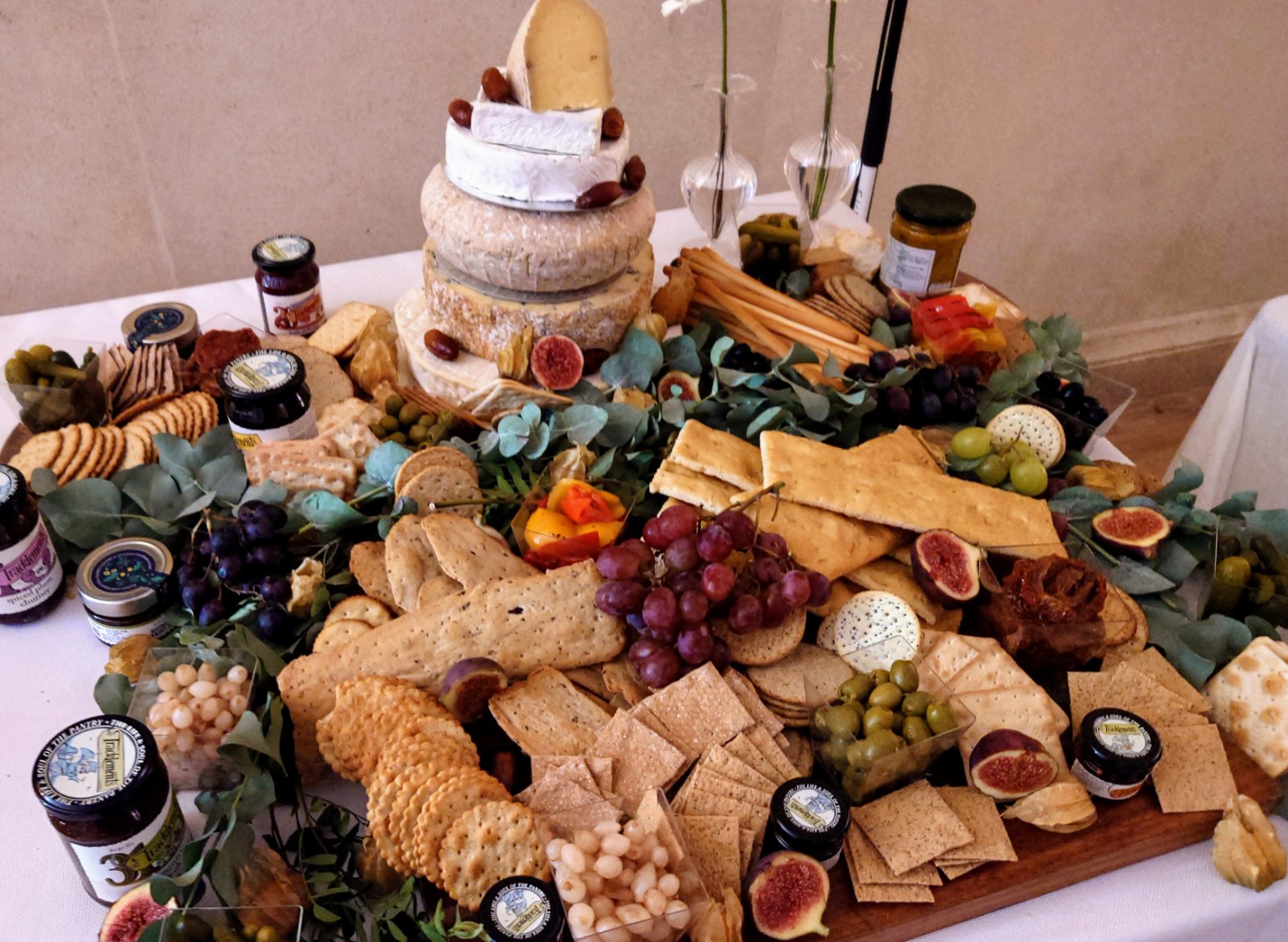 A tiered cheese centrepiece surrounded by crackers, grapes, figs and chutneys